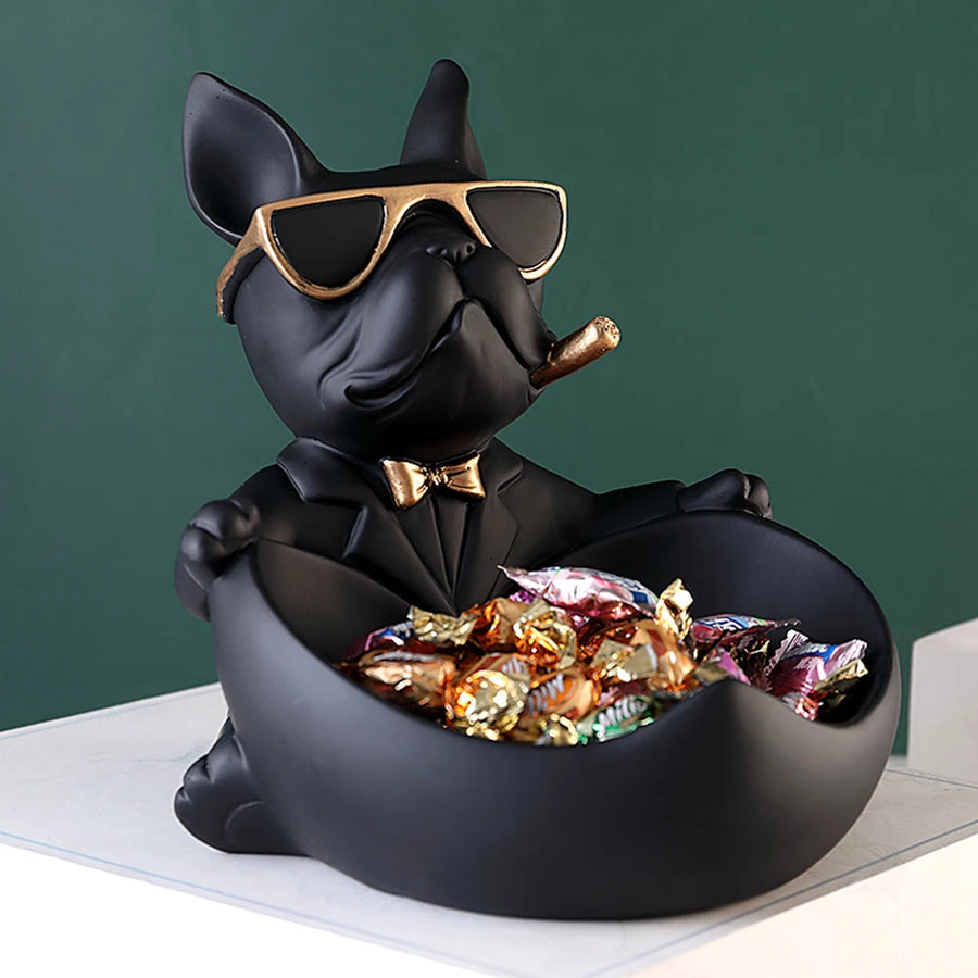 Black dog figurine with sunglasses and bow tie holding a bowl of snacks against a green background