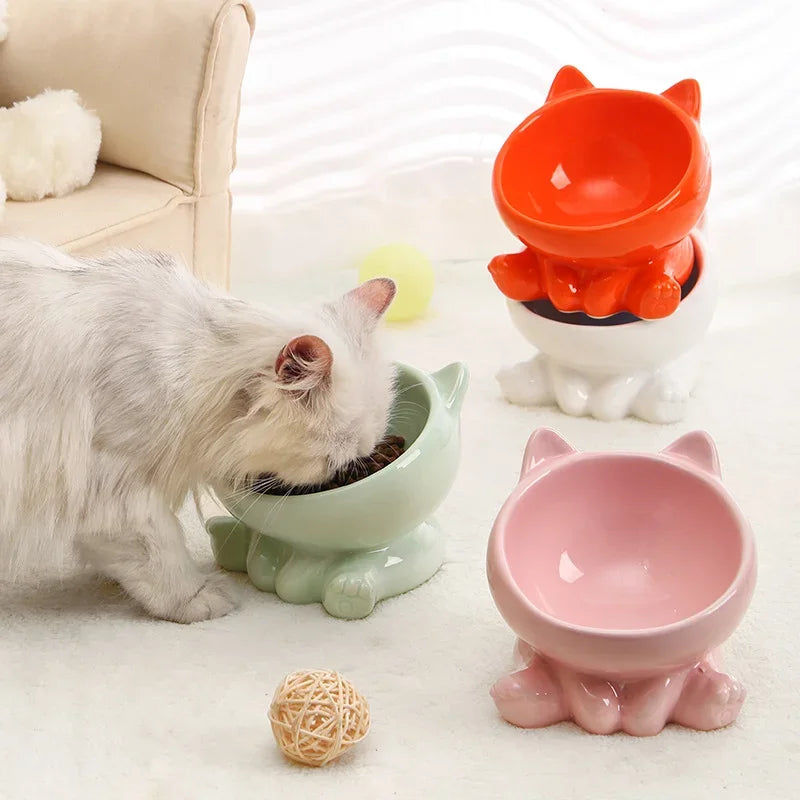 Cat eating from a green bowl with pink and orange cat-shaped bowls in the background.